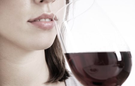 Una mujer bebiendo una copa de vino tinto.