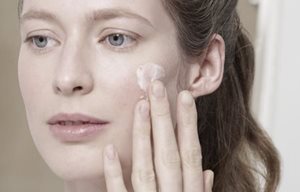 Una mujer aplicándose crema en la mejilla izquierda.