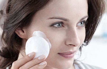 Mujer aplicándose crema en la cara con una compresa de algodón